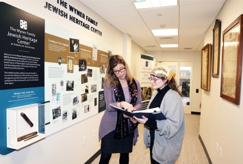 two women standing in a hallway reading archival materials