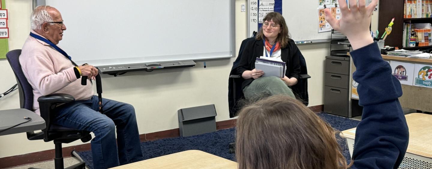 Jewish Neighborhood Voices oral historian and JHC Staff member speak in front of class; one student has raised their hand.